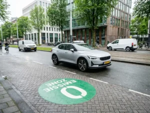 Elektrische auto rijdt door Nederlandse stadsstraat met groen nul-emissiezone-markering op het wegdek.