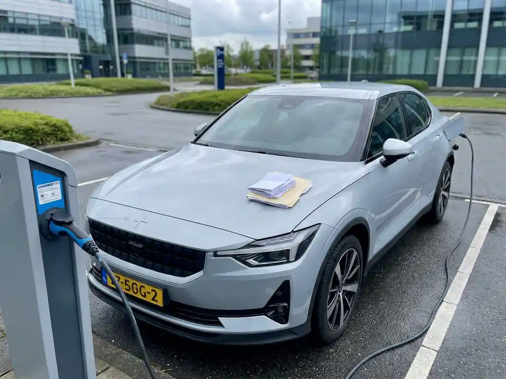 Elektrische leaseauto aangesloten op laadpaal in Nederlands bedrijventerrein, met administratieve documenten op de motorkap.