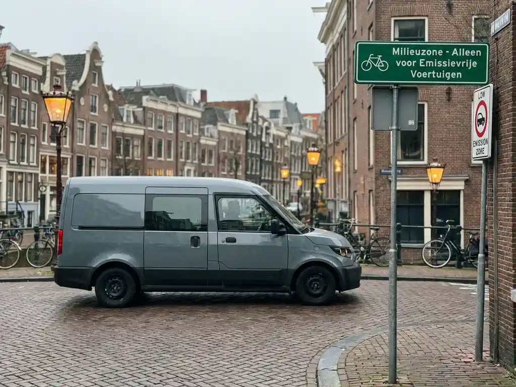 Moderne bezorgbus bij de grens van een stedelijke lage-emissiezone in een Nederlandse stad, met groen straatbord en kanaalbebouwing op de achtergrond.