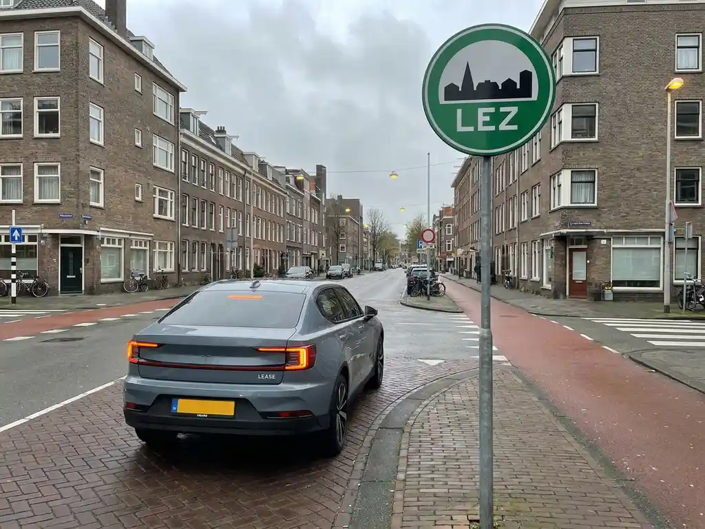 Leaseauto voor een milieuzonebordje in een Nederlandse stad met fietspaden en bakstenen gevels.