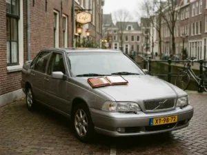 Zilveren sedan uit de late jaren negentig geparkeerd op een Nederlandse straat met een leasecontract op de motorkap.