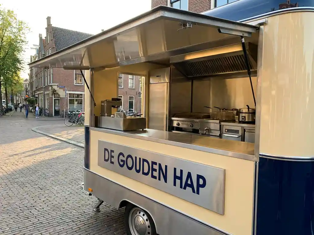 Professionele foodtruck met open servicevenster en roestvrijstalen keukenapparatuur, geparkeerd op een zonnige Nederlandse straat in warm middaglicht.