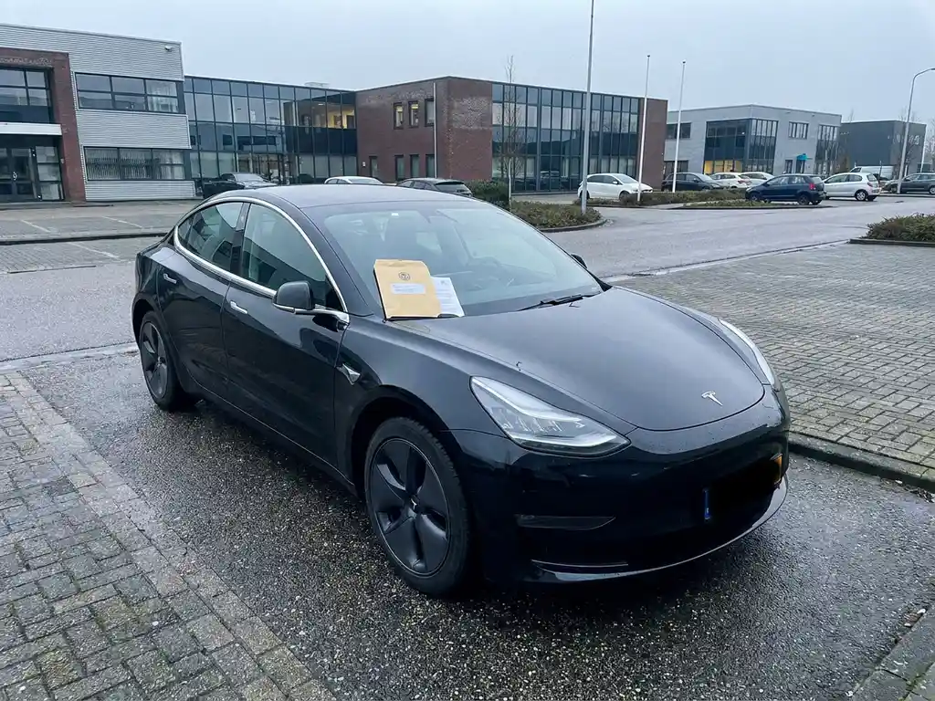 Zwarte leaseauto geparkeerd op Nederlands bedrijventerrein met officieel document op de motorkap, bewolkt daglicht.